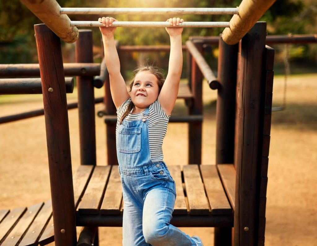 a young girl in overalls playing on the monkey bars