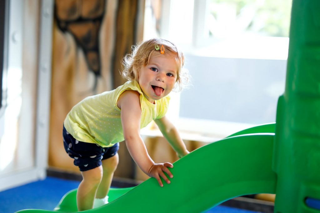 a toddler playing on a slide and sticking her tongue out