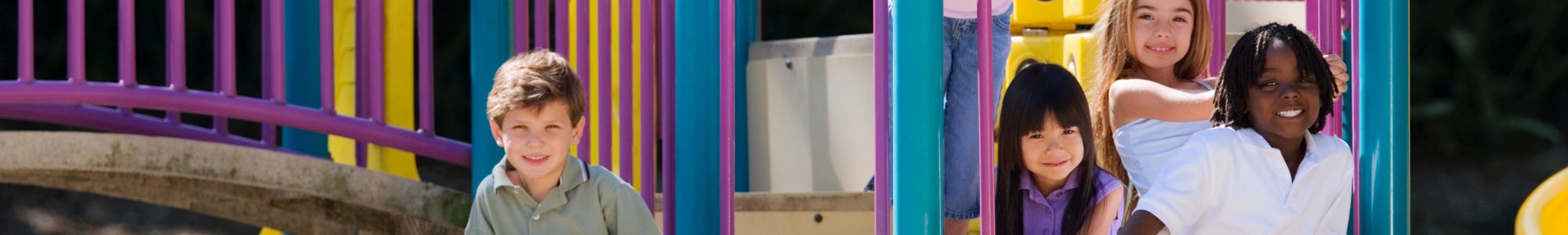 A purple, blue and yellow playground with a bunch of young children on it, looking into a camera.