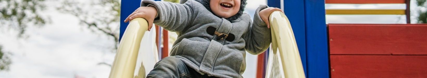 A young kid about to slide down a slide with a smile on his face.