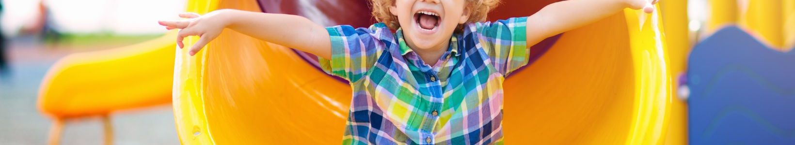 A young child at the bottom of a slide with a big smile.