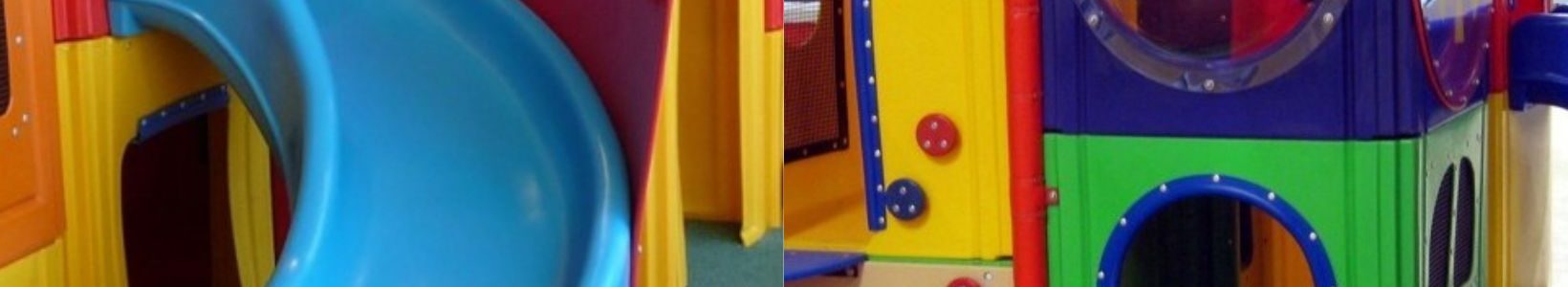 Colorful indoor playground with a blue slide, red and yellow play structures, and a circular window, creating a vibrant and playful atmosphere.
